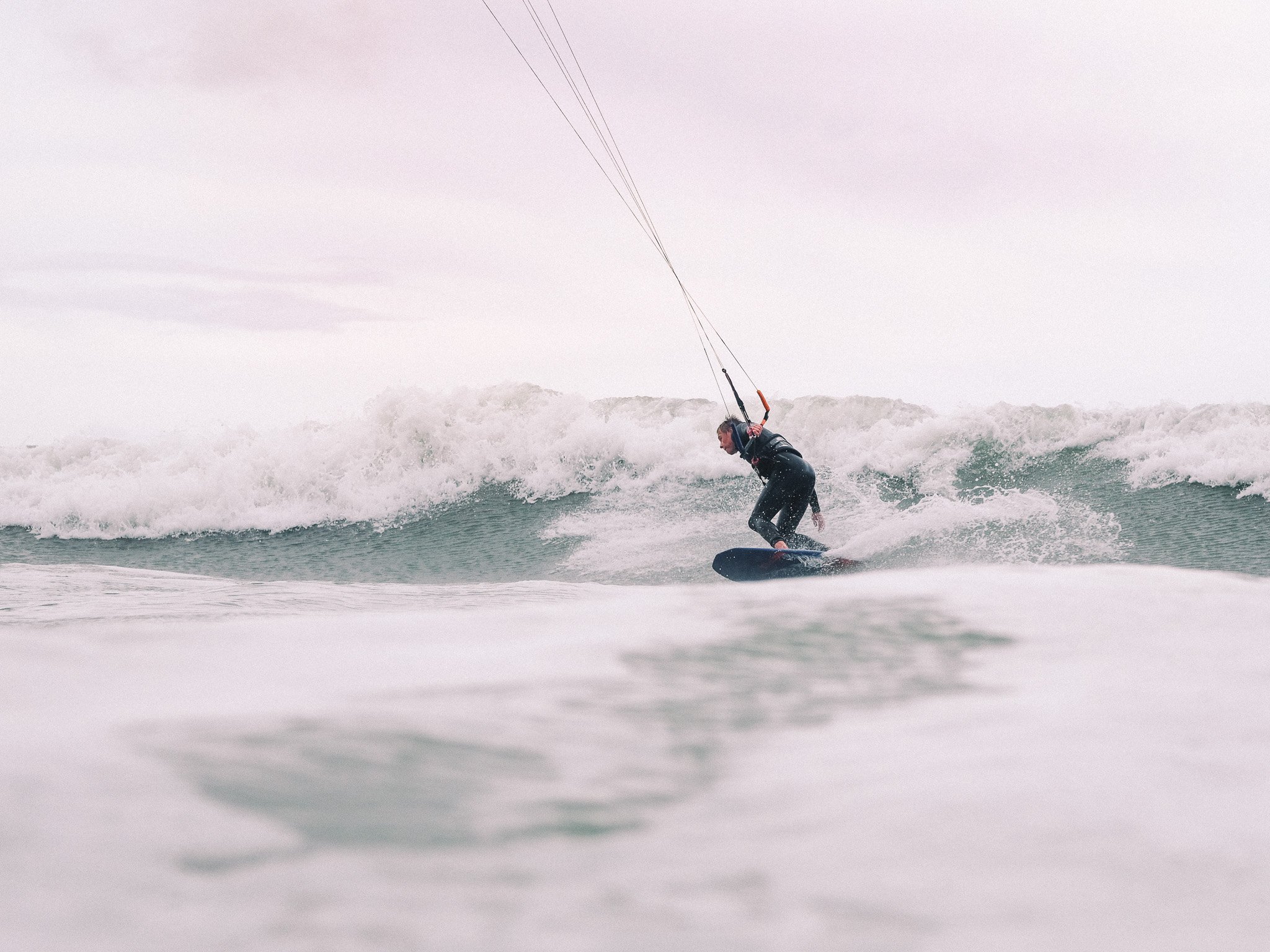 Person kite surfing on ocean waves in overcast weather.