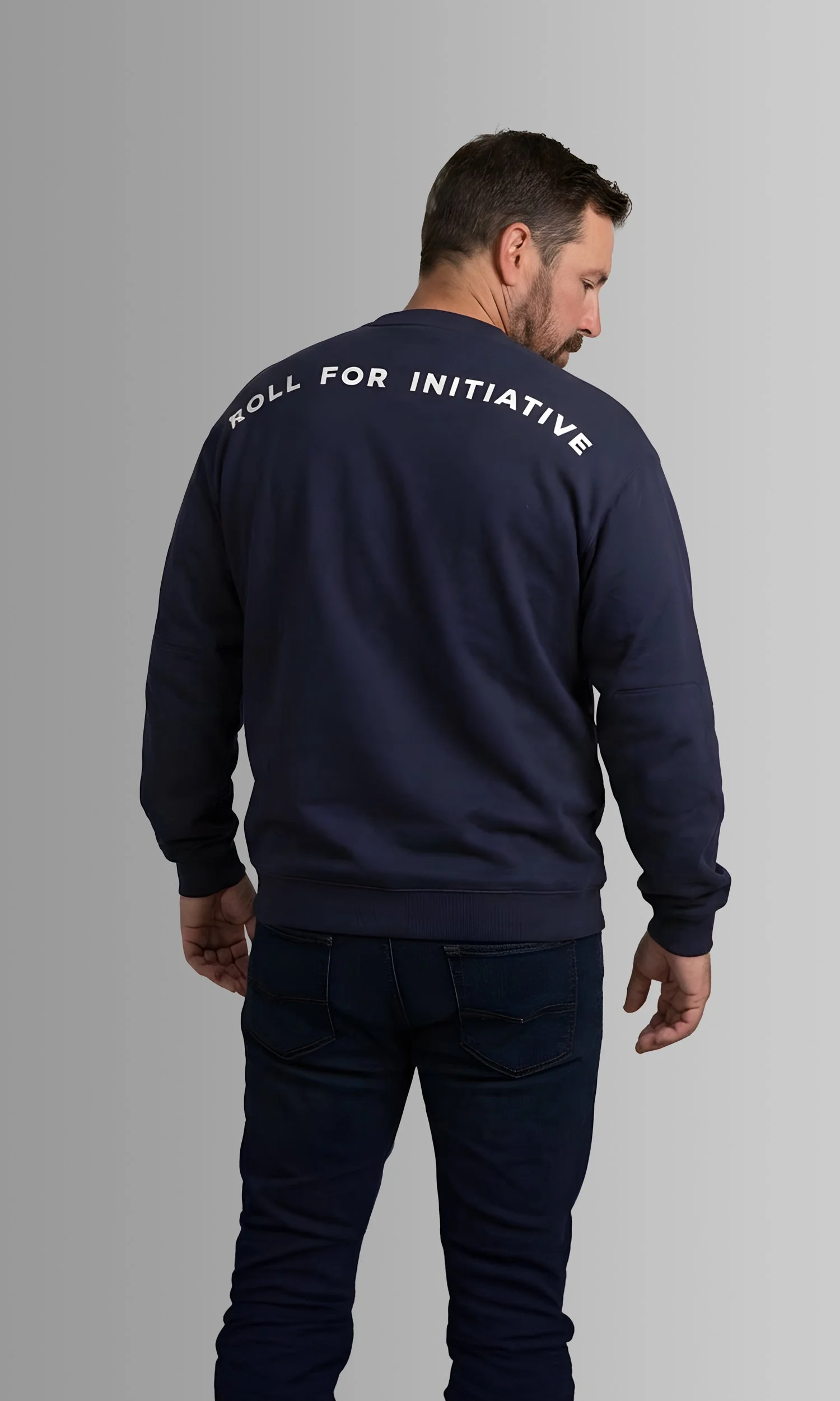 Man wearing black sweatshirt with white text 'ROLL FOR INITIATIVE' on the back, standing against a gray background, facing away and looking downward.