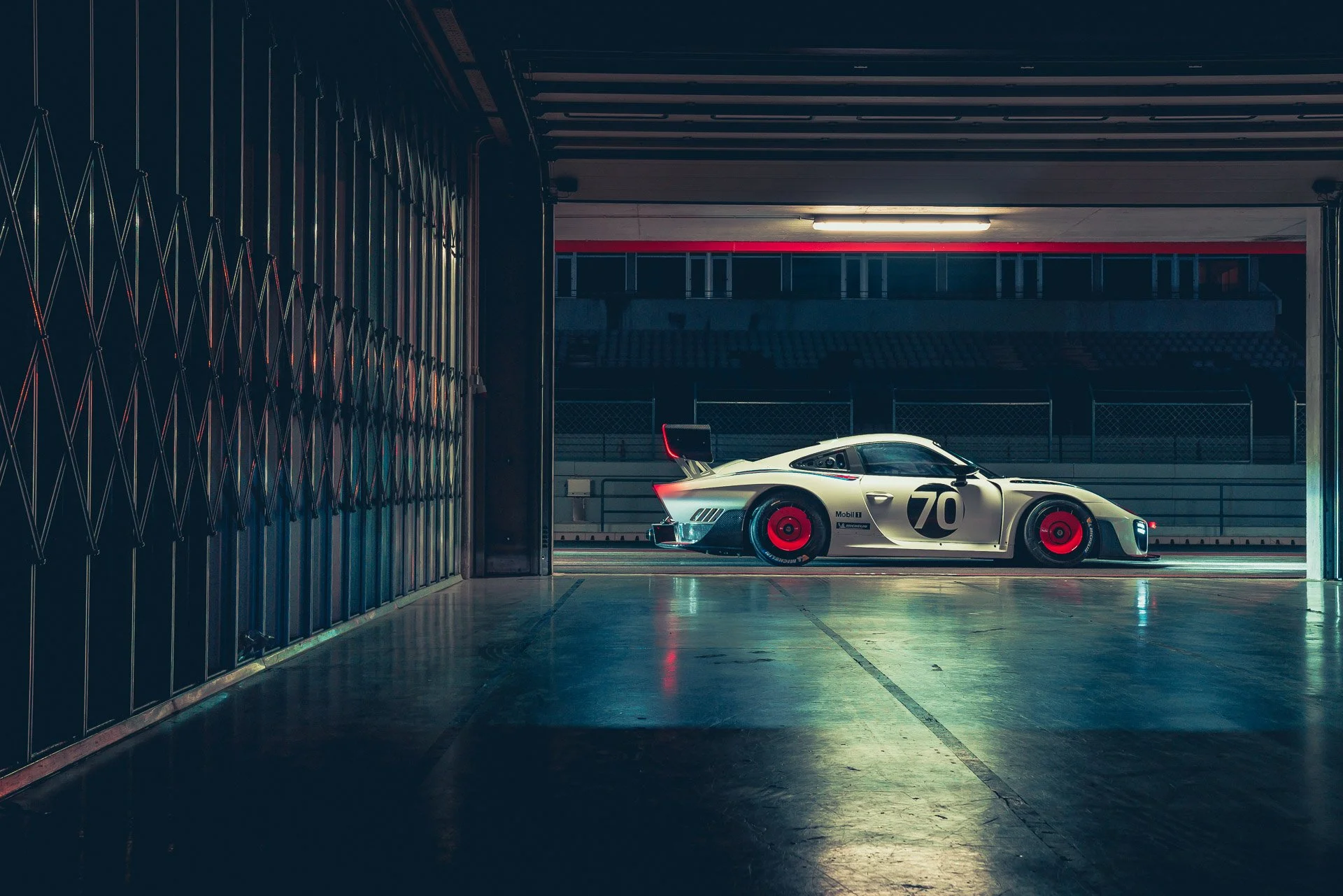 A vintage race car with the number 70 on its side, parked inside a dimly lit garage at a race track.