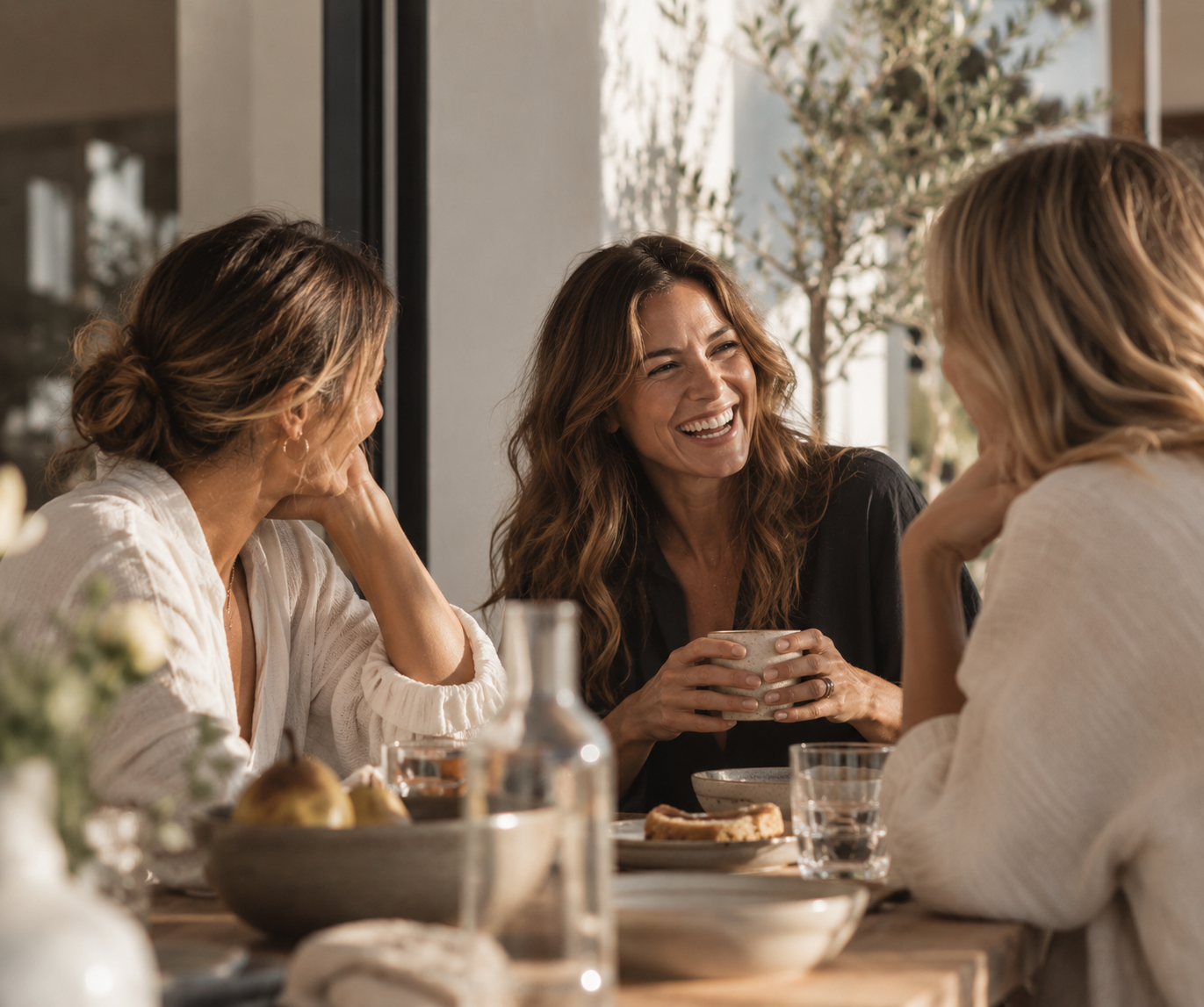 Three women enjoying a meal and conversation at a dining table, smiling and laughing together.