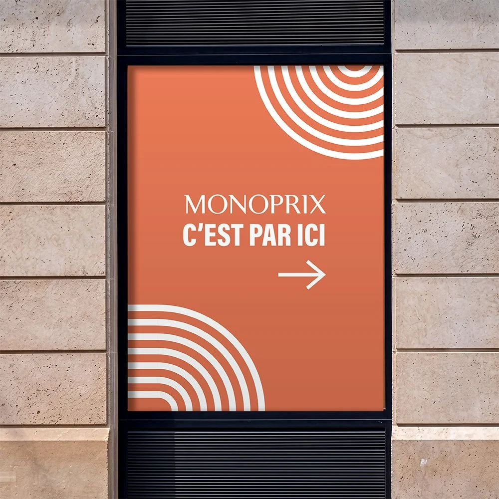 Panneau indiquant que le Monoprix se trouve ici, avec une flèche pointant vers la droite et un fond orange avec des motifs de cercles blancs.