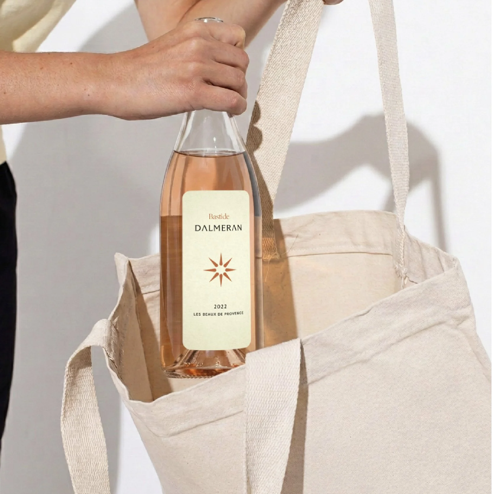 Une bouteille de rosé Rosé Dalmeran de la récolte 2022, avec une étiquette blanche contenant un symbole en forme d'étoile et les mots "Les Beaux de Provence", placée dans un sac en tissu beige.