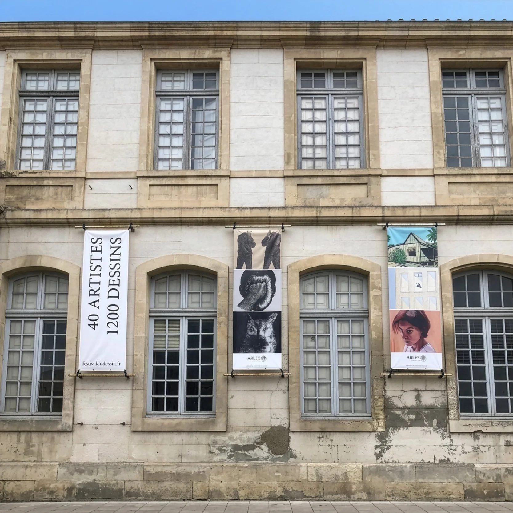 Façade en pierre habillée de bannières « 40 artistes, 1200 dessins », communication extérieure du Festival du dessin à Arles