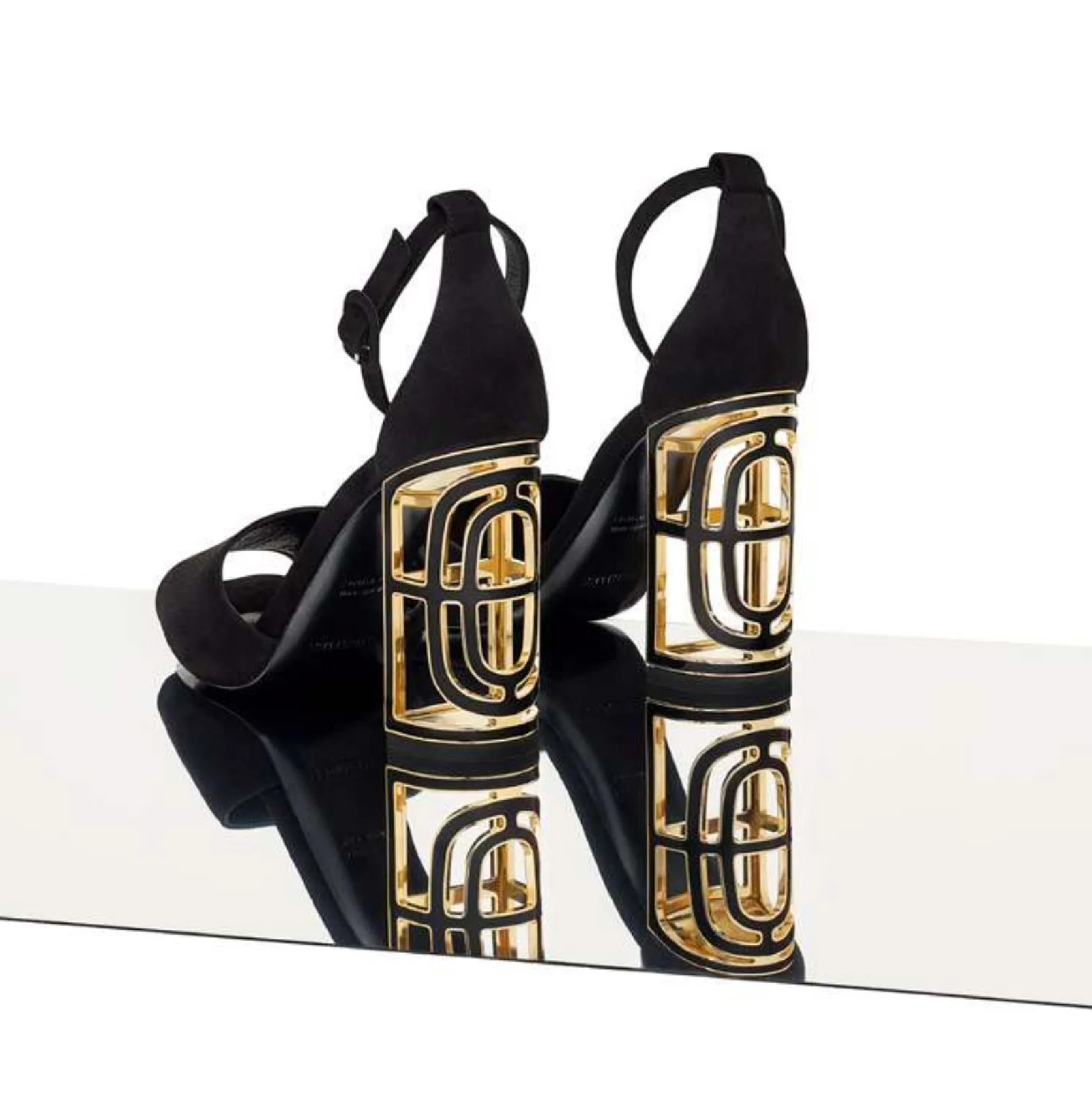 Sandales Hermès noires à talon doré ajouré, reflet sur surface miroir et fond blanc