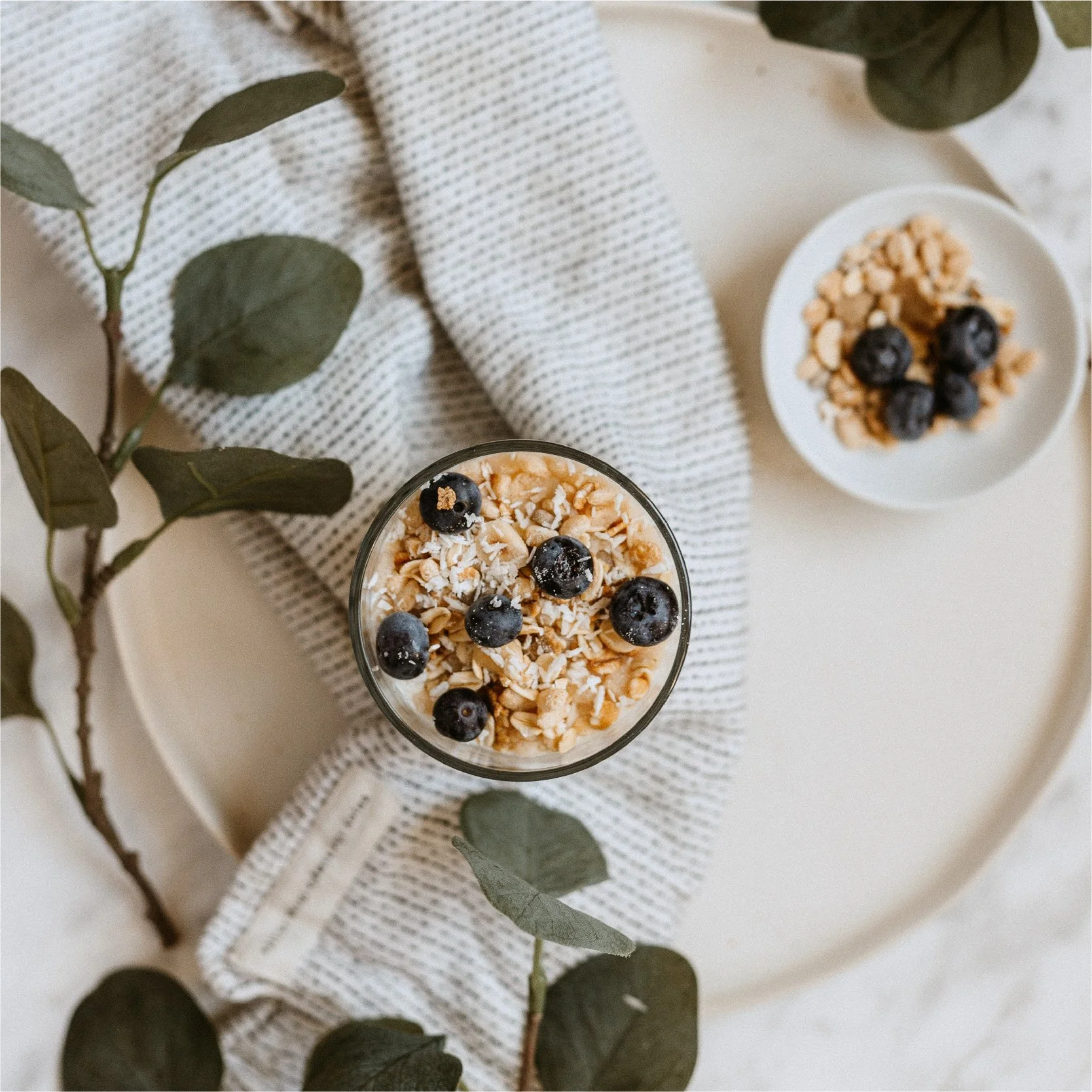 Photographie culinaire d'un bol de flocons d'avoine aux myrtilles sur assiette, feuillage et textile beige, univers visuel Bespoke by Sunday