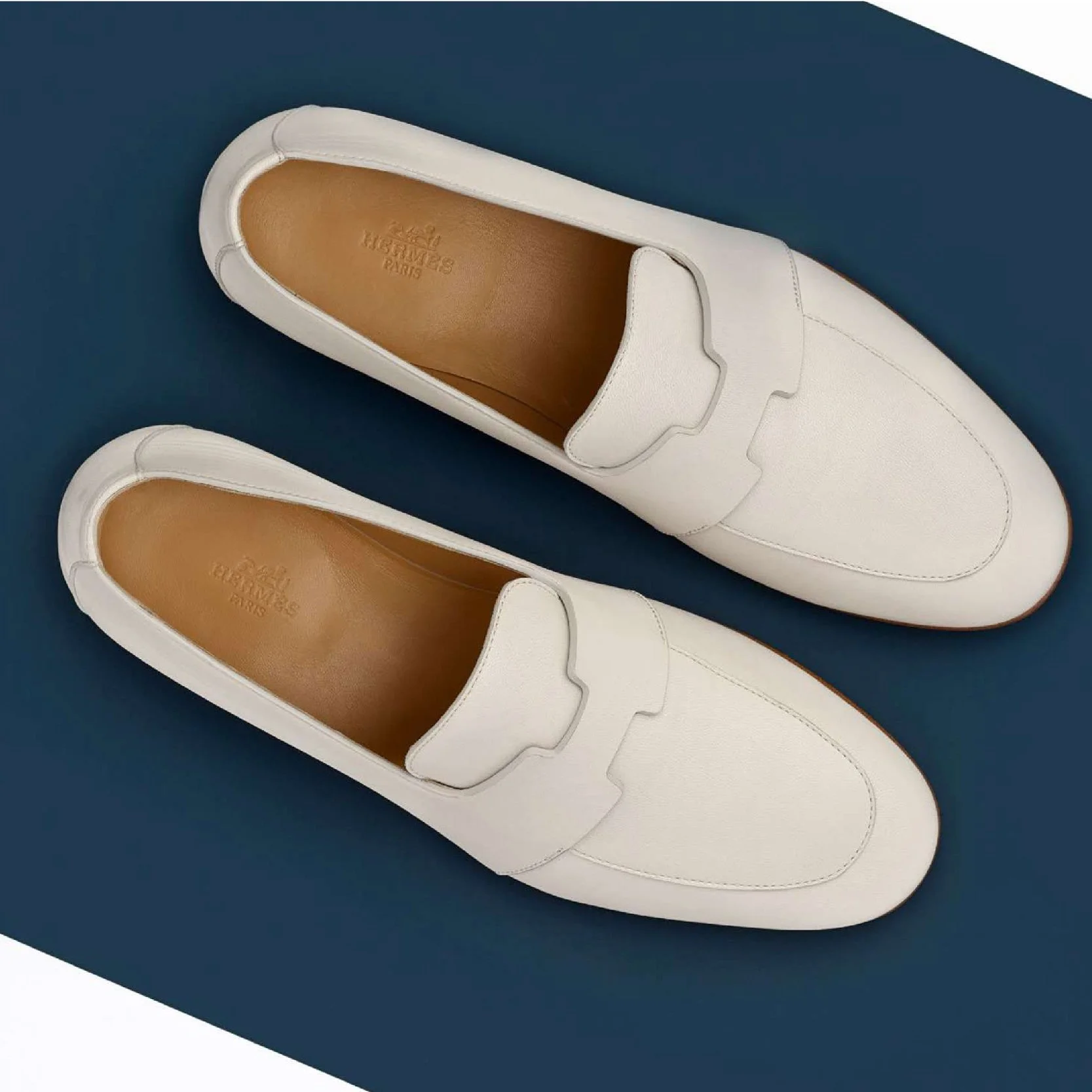 Paire de mocassins Hermès blancs vus du dessus sur fond bleu marine découpé en diagonale