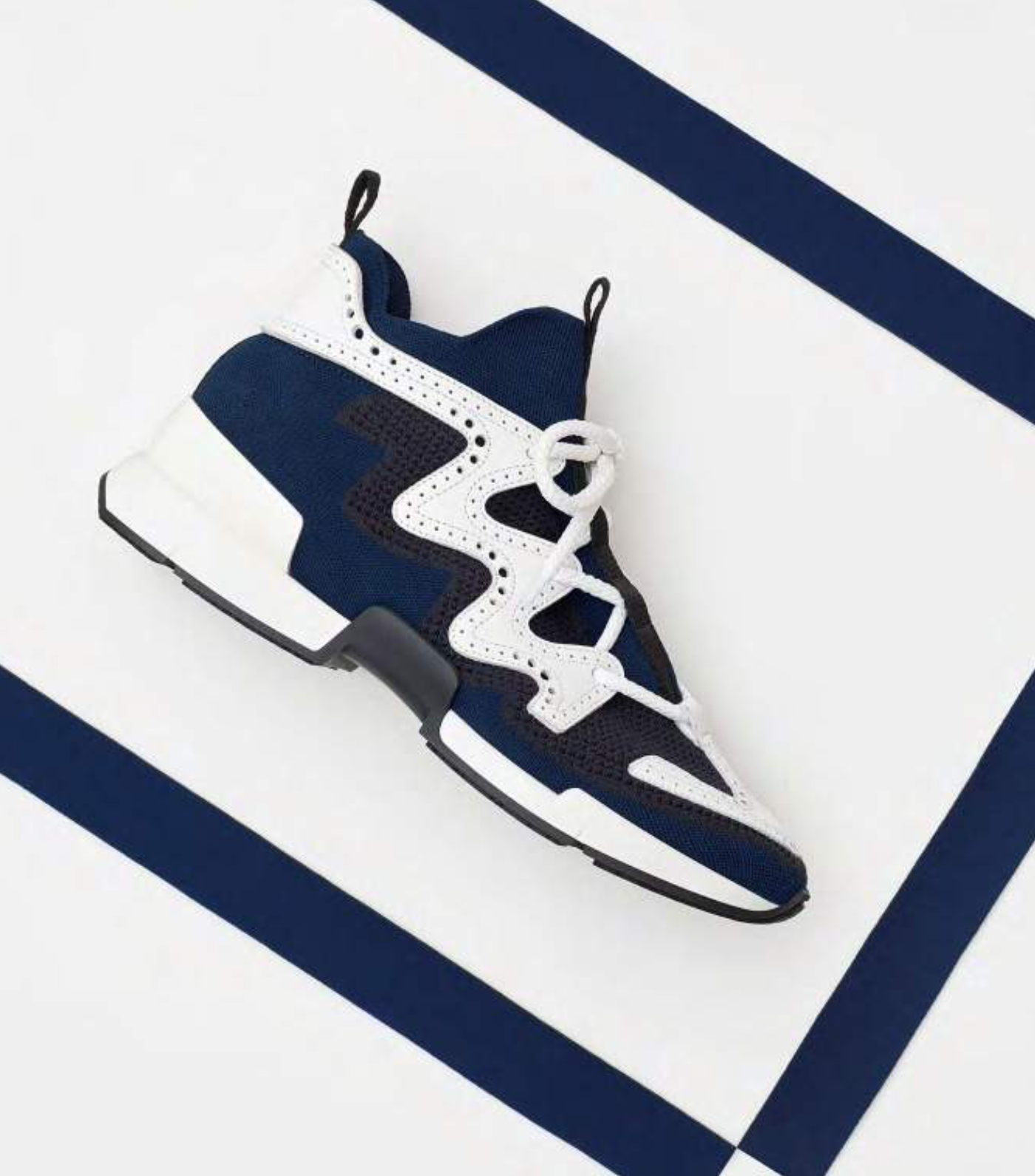 Une chaussure de sport moderne de couleur noire, blanche et bleue, posée sur un fond de motifs géométriques bleu et blanc.