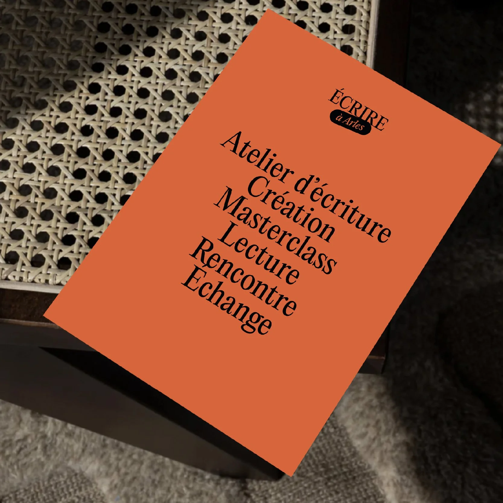 Affiche orange « Atelier d'écriture, Création, Masterclass, Lecture, Rencontre, Échange » posée sur une assise en cannage, identité Écrire à Arles