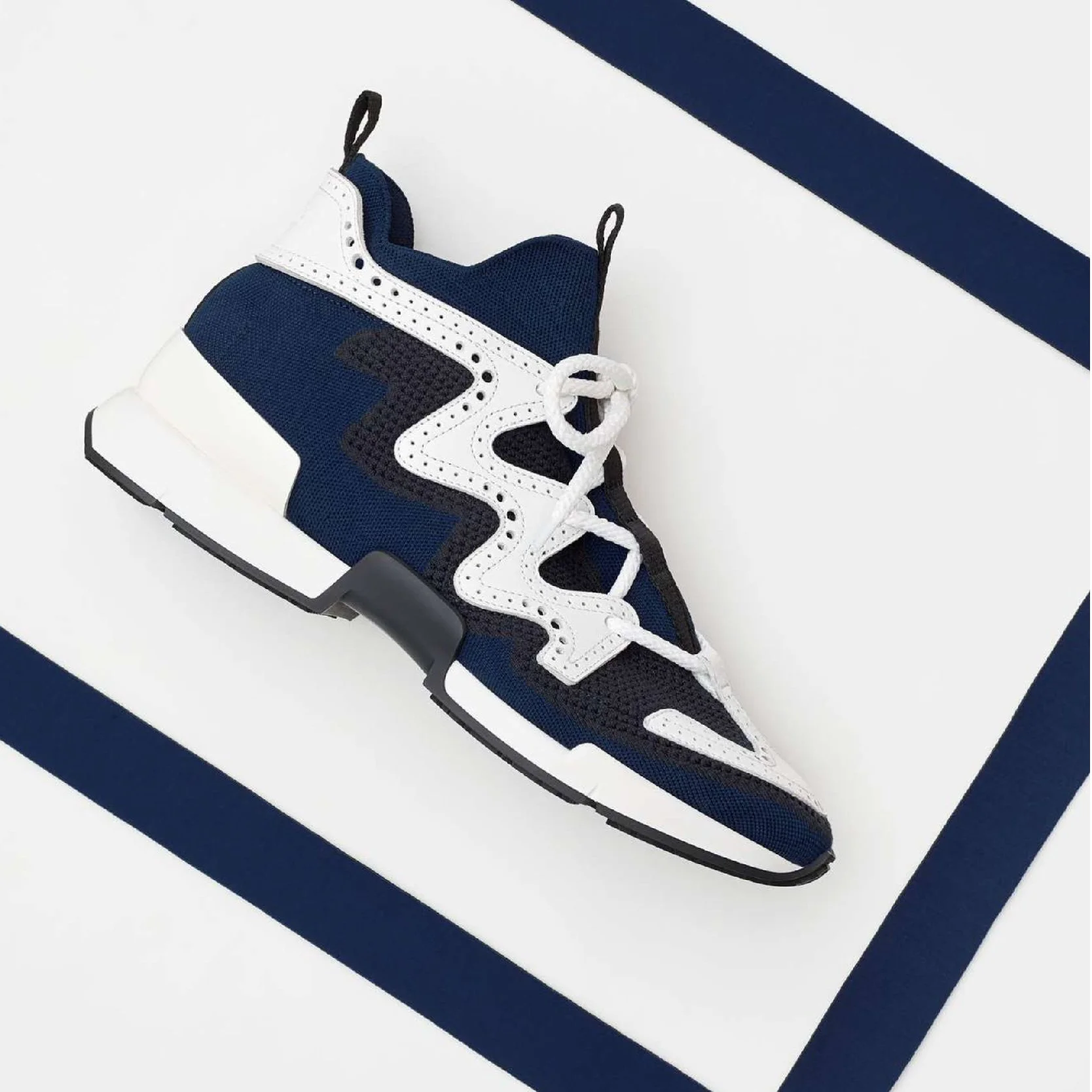 Un sneaker de sport de couleur bleue, noire et blanche placé sur un fond blanc avec une bande noire diagonale