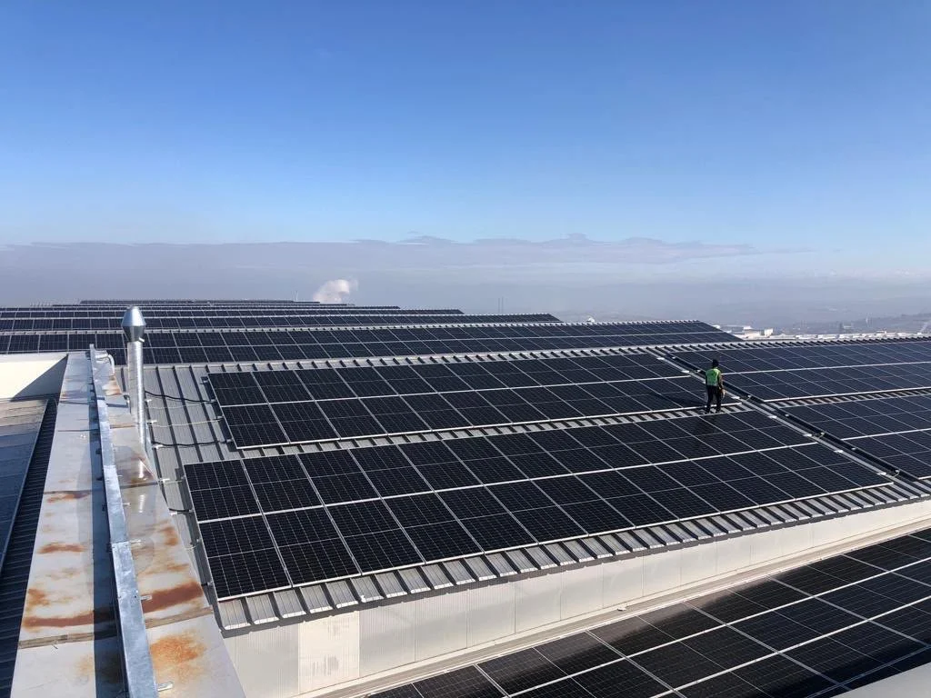 Güneş enerjisi panelleriyle kaplı bir çatı, gökyüzü ve bulutlar.