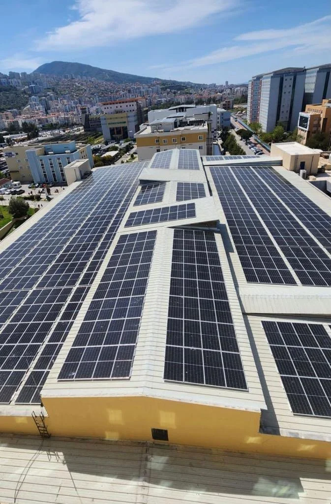 Güneş panelleriyle kaplı bir çatının üzerinde şehir ve dağ manzarası.