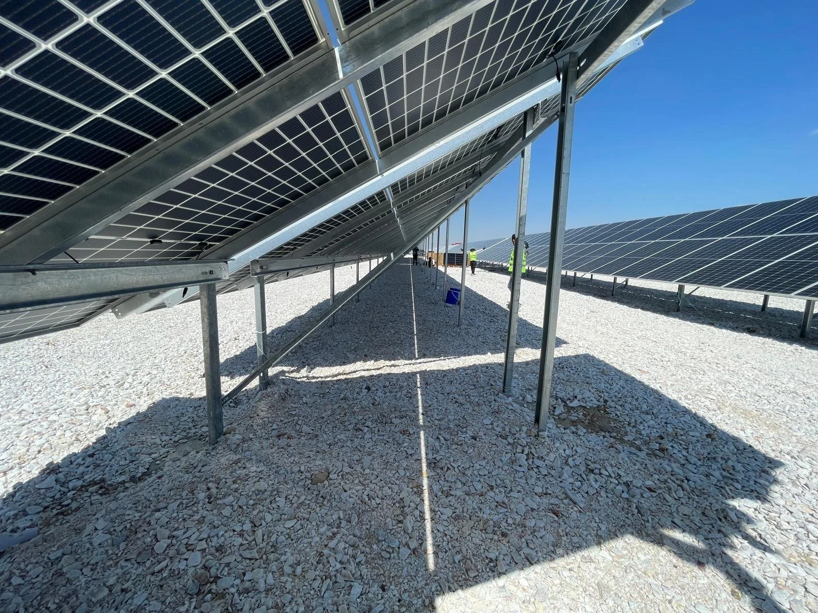 Güneş enerjisi panelleriyle donatılmış bir güneş enerji santrali, açık gökyüzü altında, panellerin altında ve çevresinde çalışanlar.