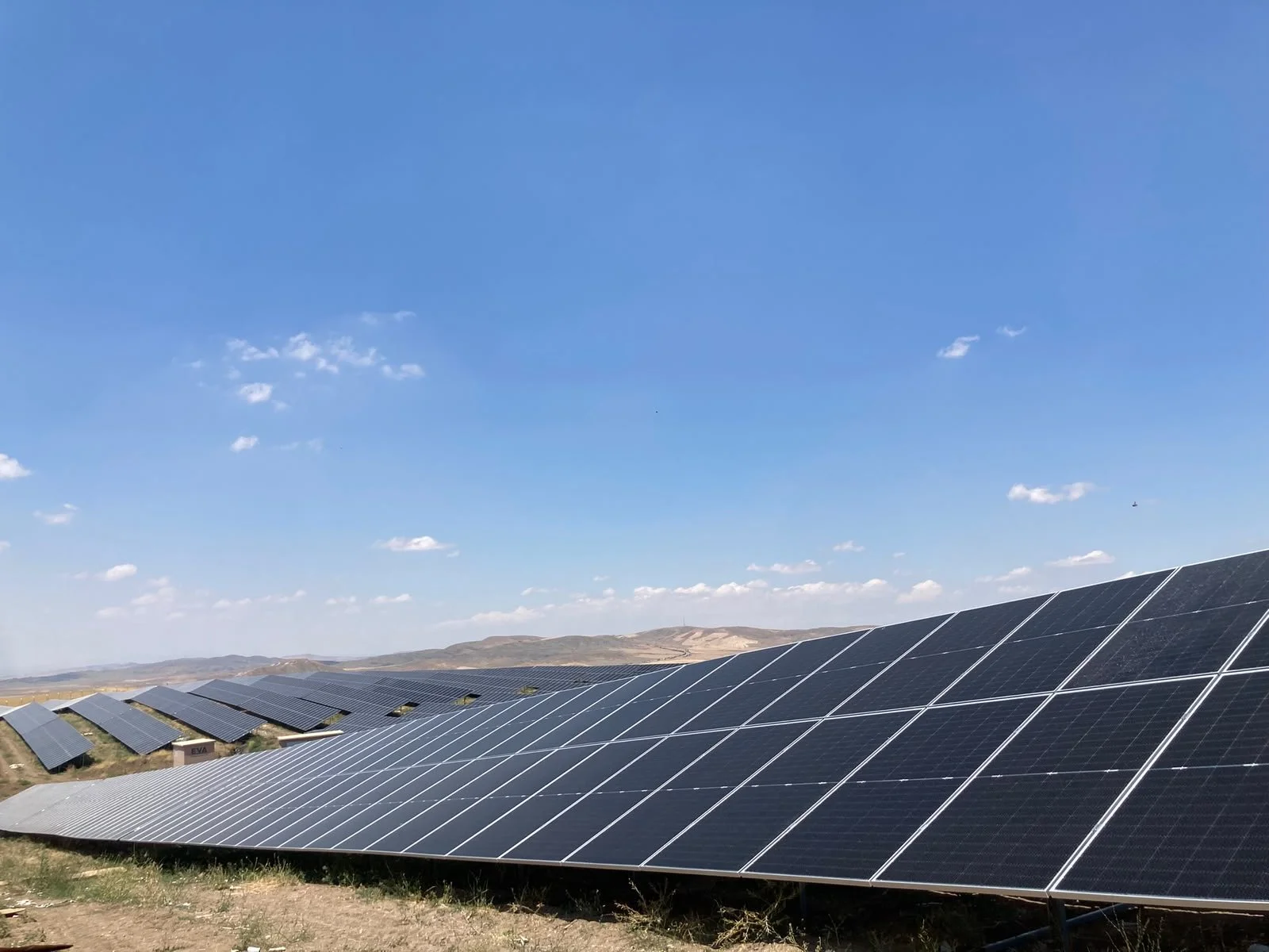 Güneş enerjisi panelleriyle dolu güneş enerjisi santrali, açık mavi gökyüzü altında, kırsal alanda kurulmuş.