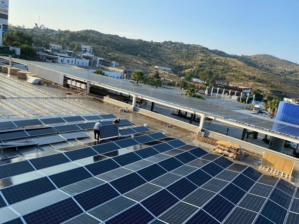 Güneş enerjisi panellerinin kurulduğu bir çatı ile şehir ve dağ manzarası.