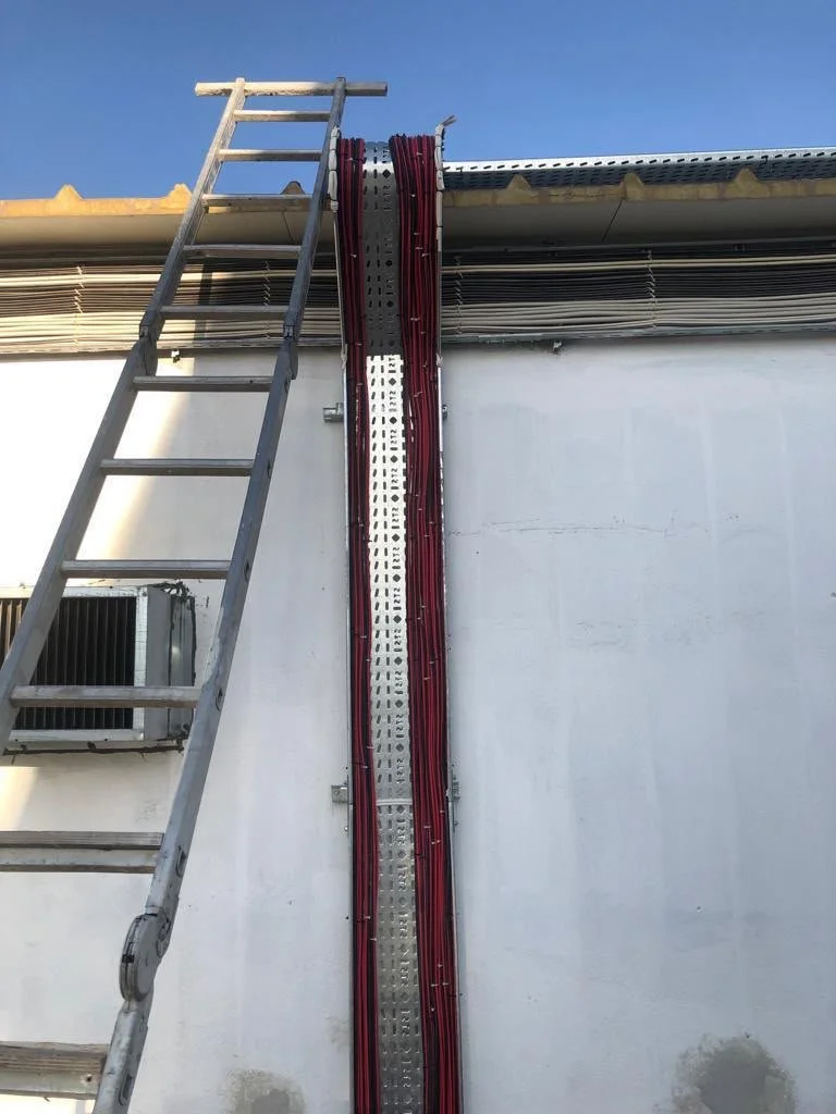 Bina dış cephesinde elektrik ve iletişim kablolarını koruyan metal altyapı ve buna bağlı sıralı kırmızı kablolar bulunmaktadır. Sol tarafta bir merdiven yer almakta.