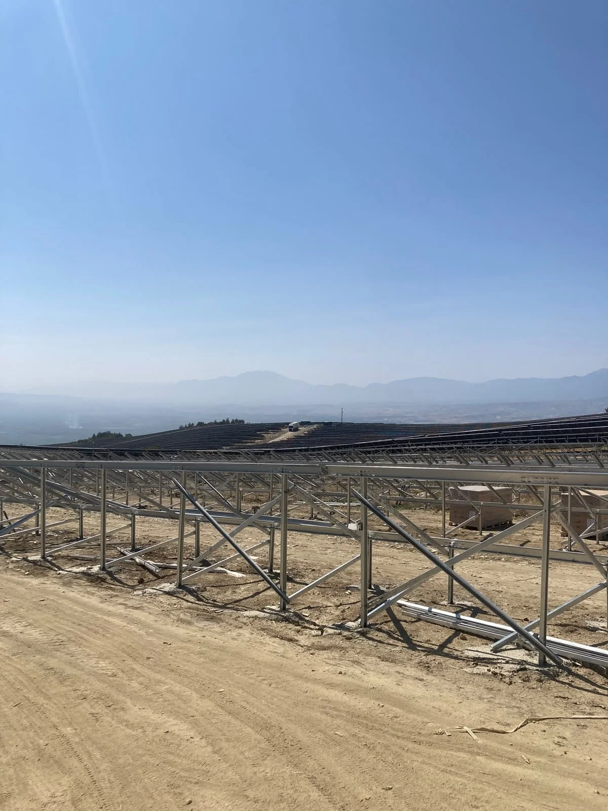 Güneş enerjisi panelleri kurulan açık bir alan, uzaklarda dağlar görünüyor.