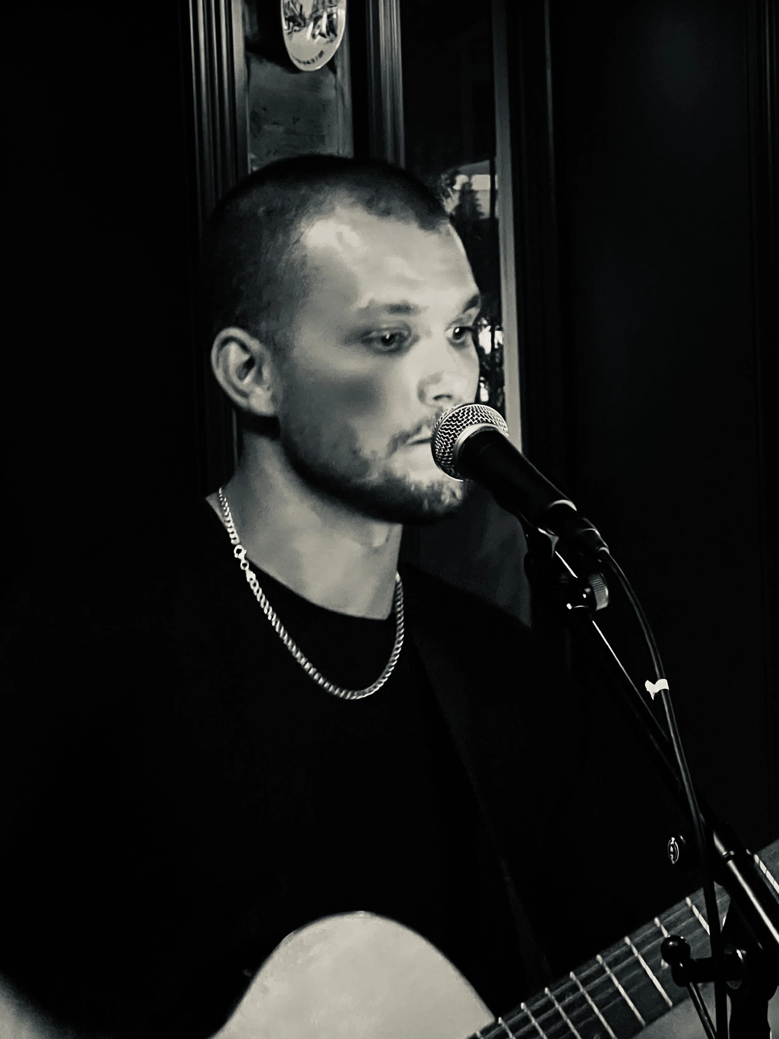 Person som spiller akustisk gitar og synger inn i mikrofonen.