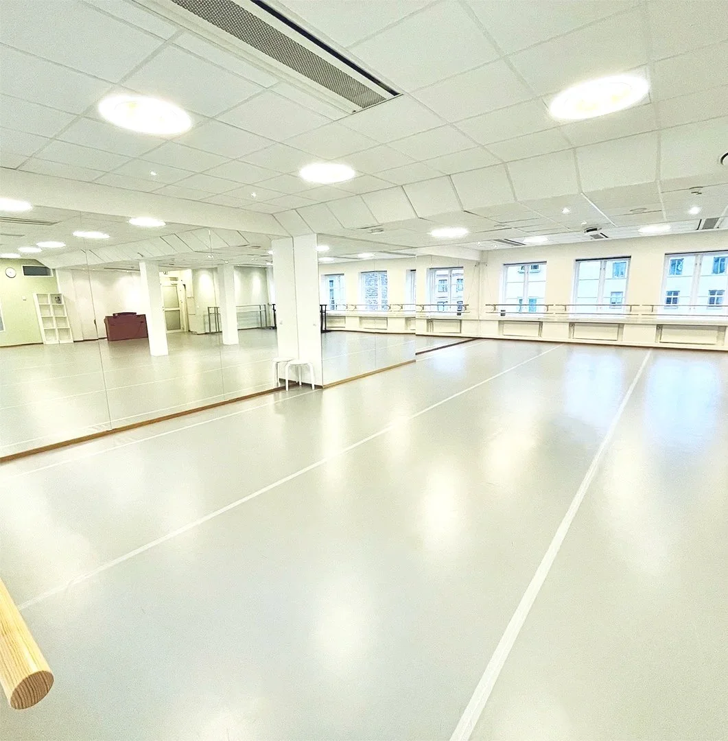 En tom danssal eller gymnastiksal med speglar på ena väggen och stora fönster på den andra vägen, belysning i taket och ett dansställe på golvet. Balettcentrum Stockholm