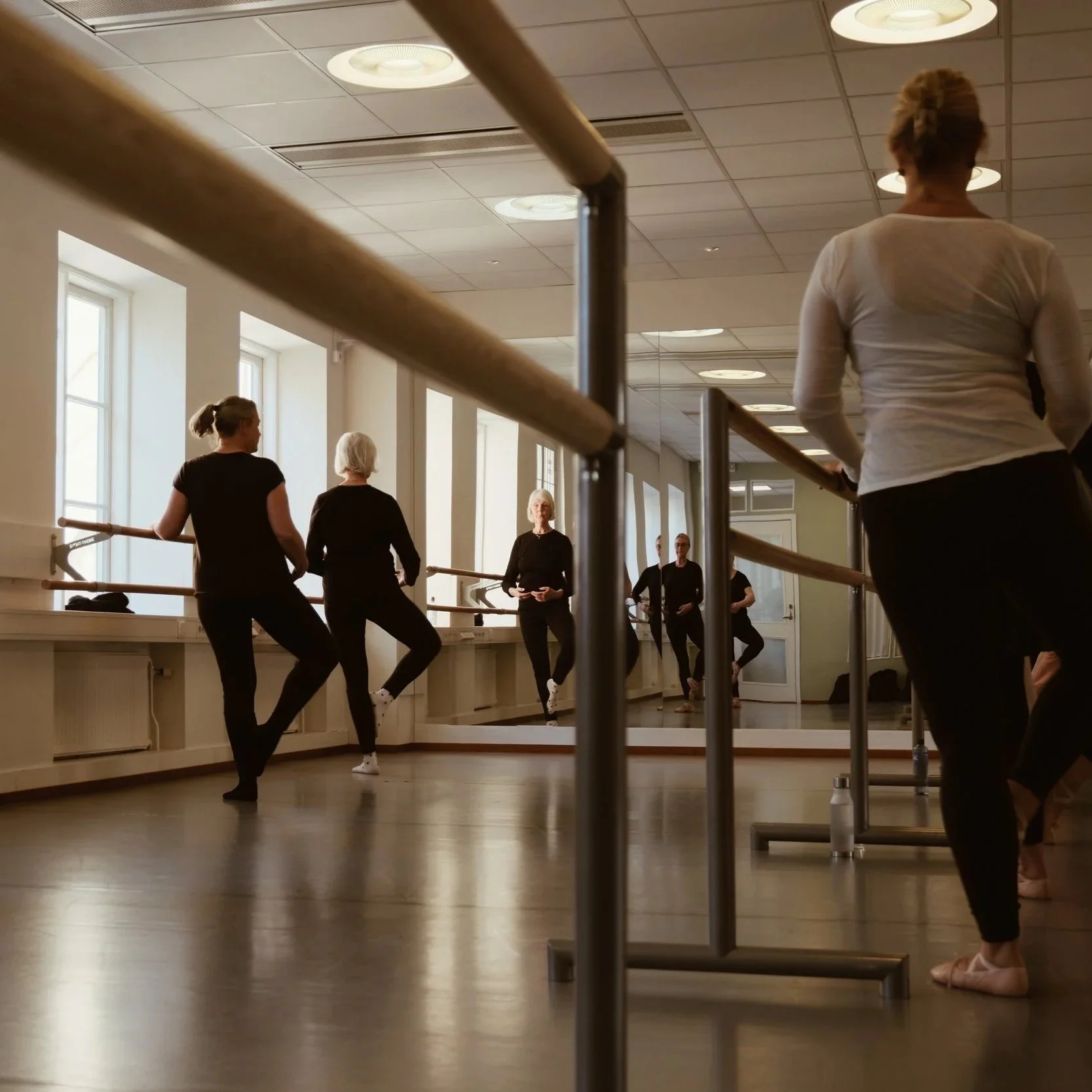 Kvinnor i träningsstudio som utövar balett vid spegelväggen.