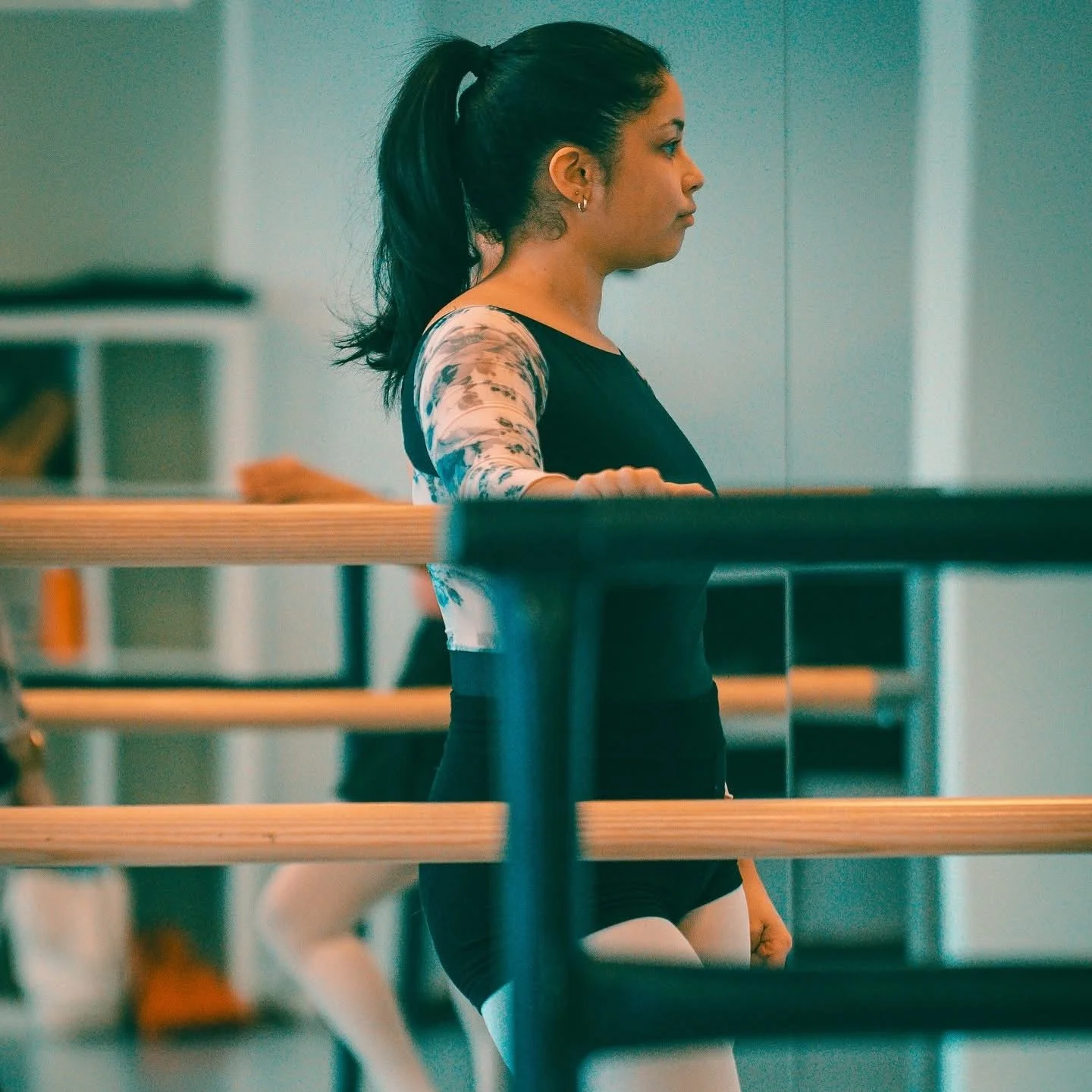 En kvinna i svart träningsdräkt och tights står vid en spegel på en träningsstudio eller dansstudio. Balettcentrum Stockholm