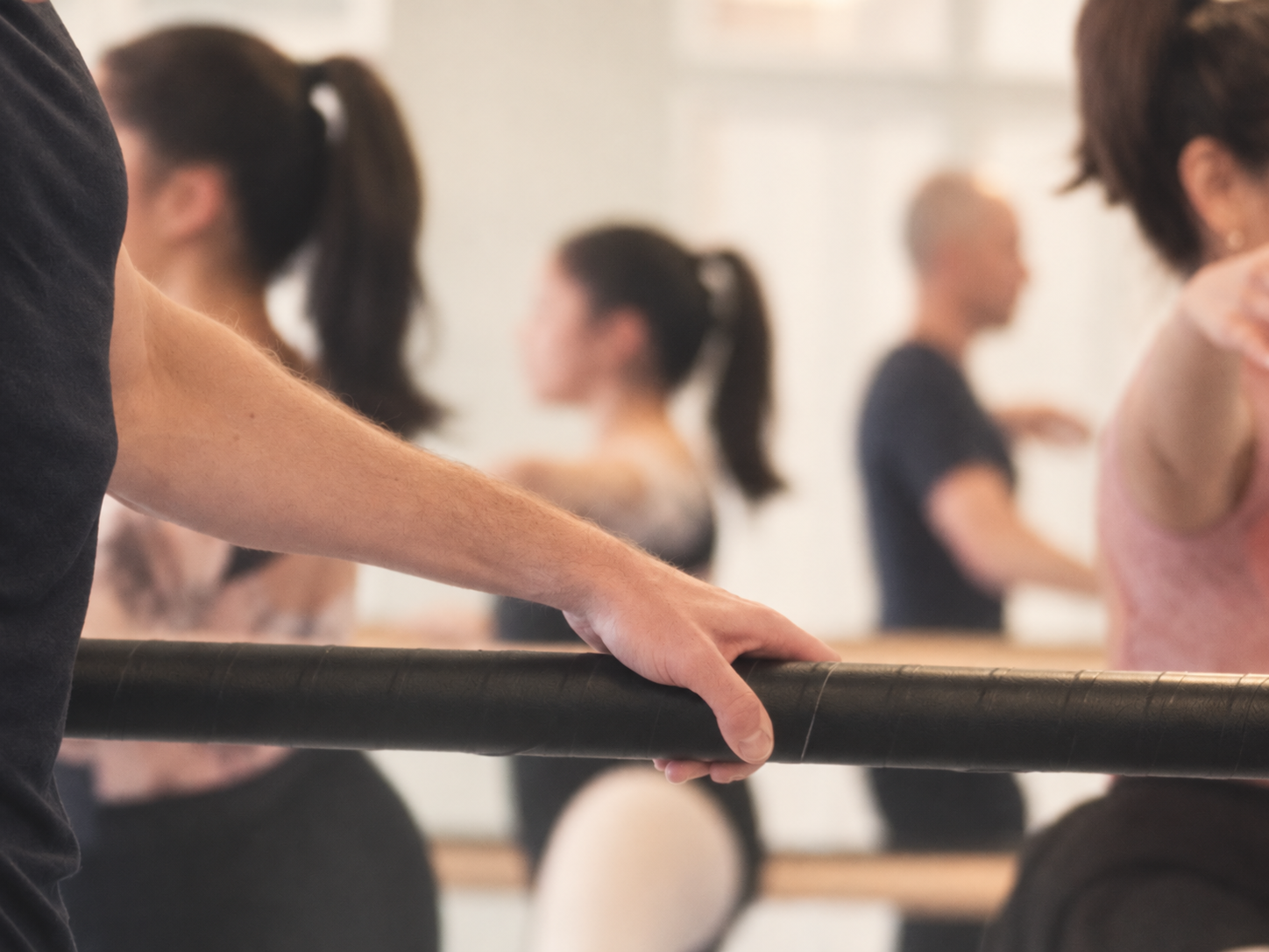 Person som håller i en balettstång i en dansstudio med flera dansare i bakgrunden. Balettcentrum Stockholm