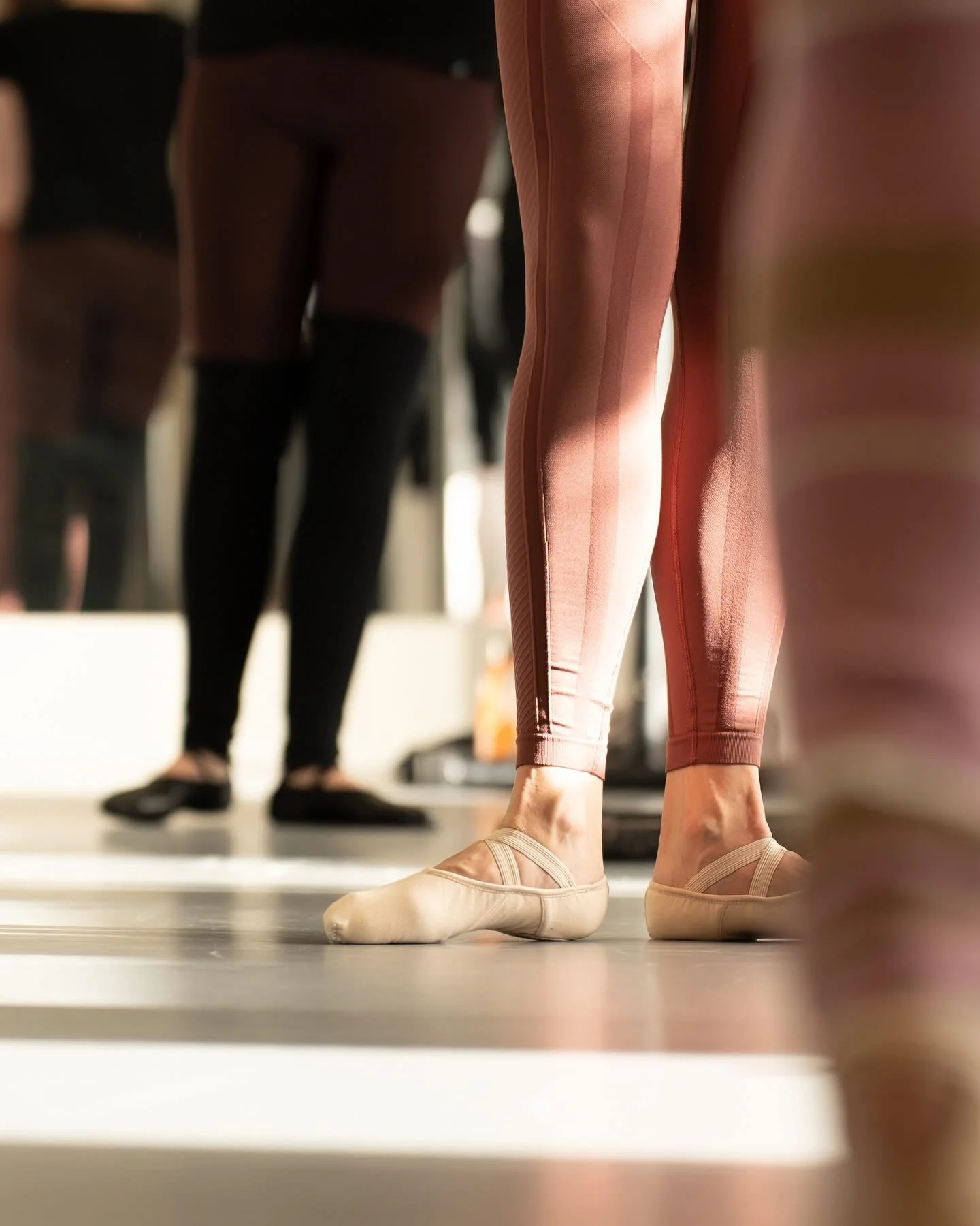 Ballerina i rosa tights och balettskor som står i balettposition i en dansstudio, andra personer i bakgrunden. Balettcentrum Stockholm