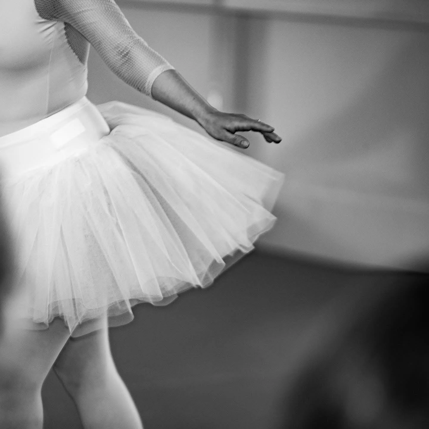 Den här bilden visar en balletdansös i vit tutu och strumpor, sittande på golvet med benen sträckta och en av hennes armar utsträckt åt sidan.