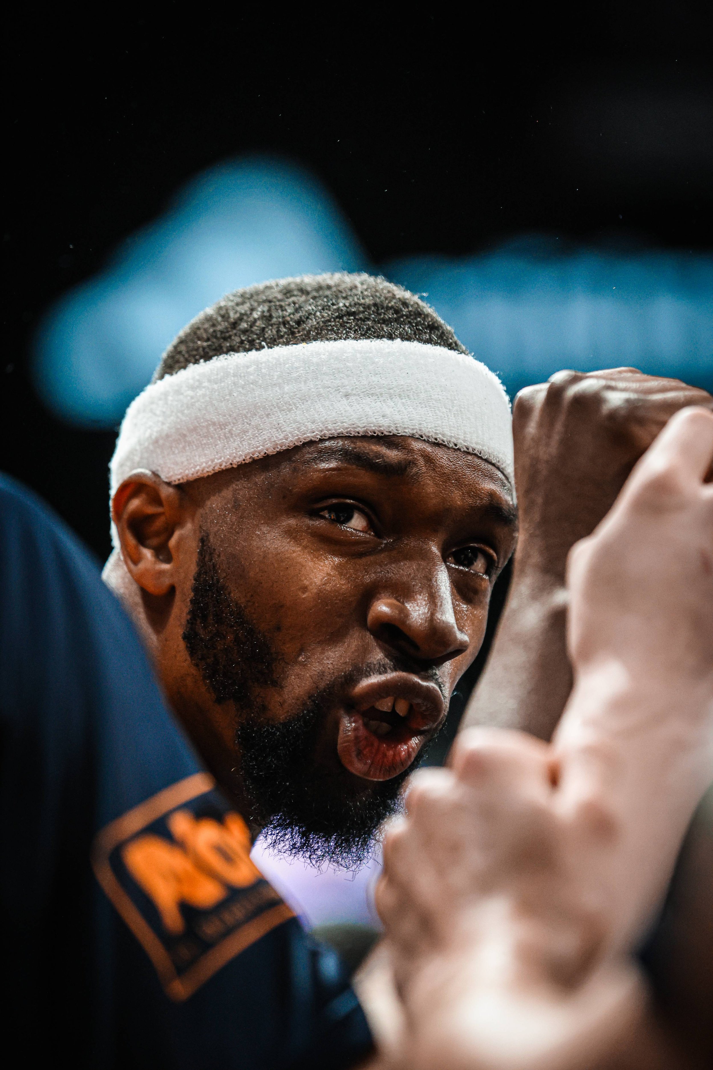 Un homme portant un bandeau blanc participe à une activité sportive ou d'entraînement, avec une expression concentrée.