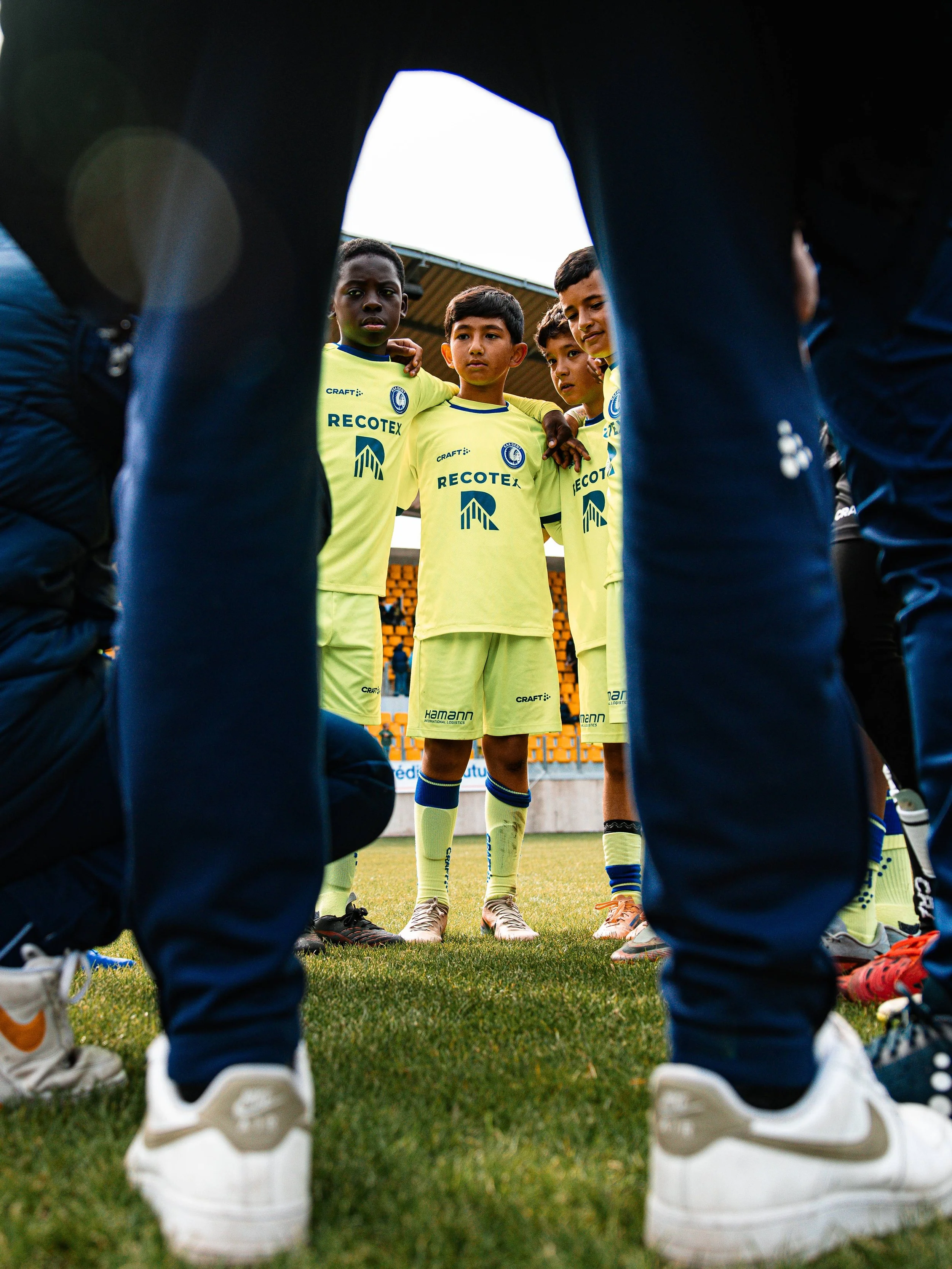 Équipe de jeunes joueurs de football en cercle lors d'une réunion d'équipe, vue à travers leurs jambes.
