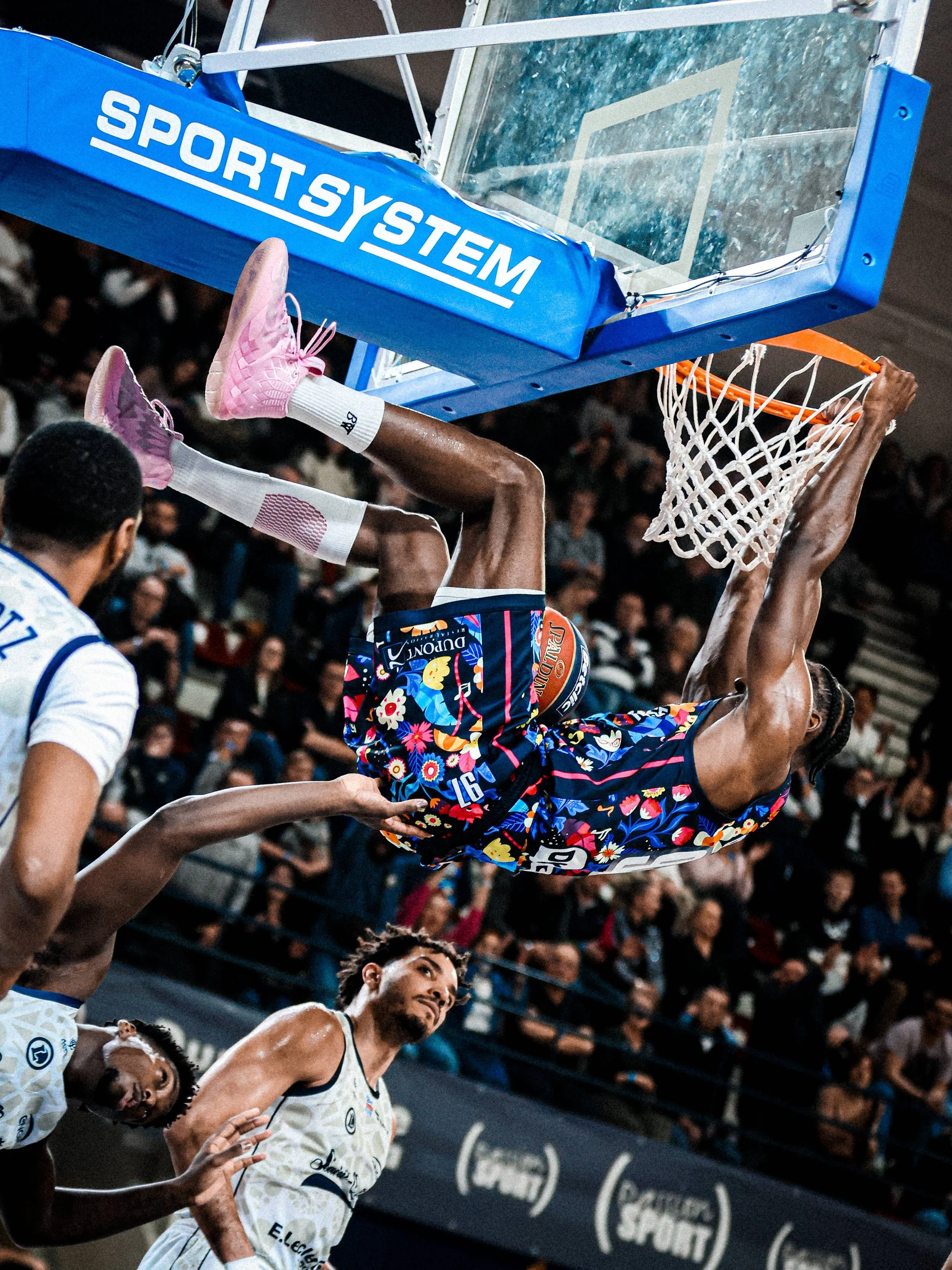 Un joueur de basketball en train de dunker lors d'un match, avec un public dans les gradins en arrière-plan.