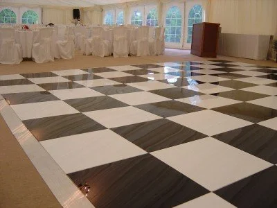 Checkered dance floor in an event tent with round tables covered in white tablecloths and chairs.