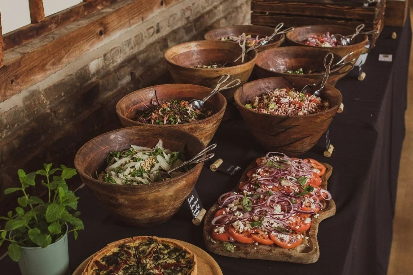 Buffet table with wooden bowls of salads and sliced tomato platter