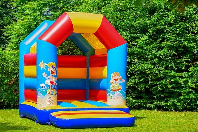 Colorful inflatable bounce house on grass with cartoon graphics and a lush green background.