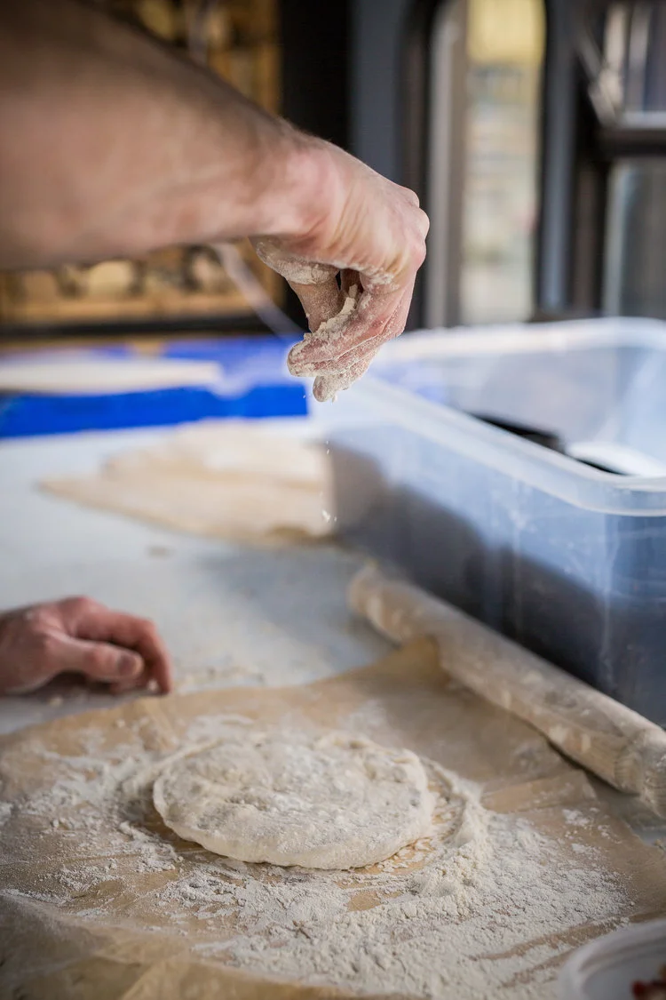 Person dusting flour on dough with a rolling pin nearby