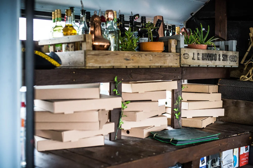 Wooden shelves with bottles, pizza boxes, and potted plants