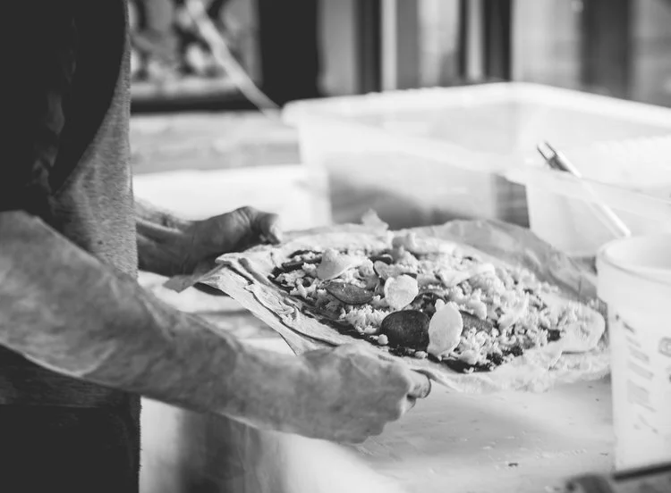 Person handling a freshly made pizza with toppings in a kitchen.