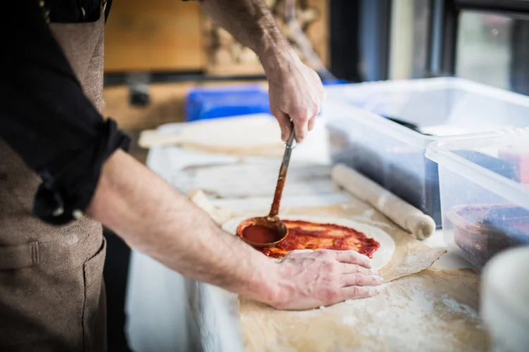 Spreading tomato sauce over a pizza base in the Fables kitchen.