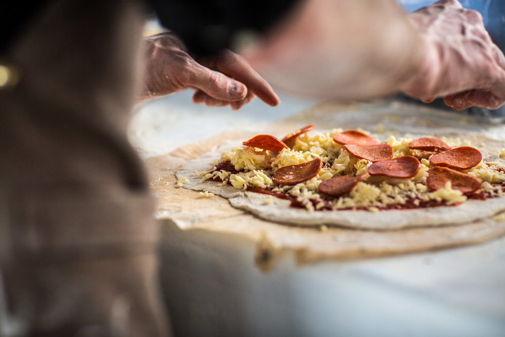 Person preparing a pizza with cheese and pepperoni on uncooked dough.