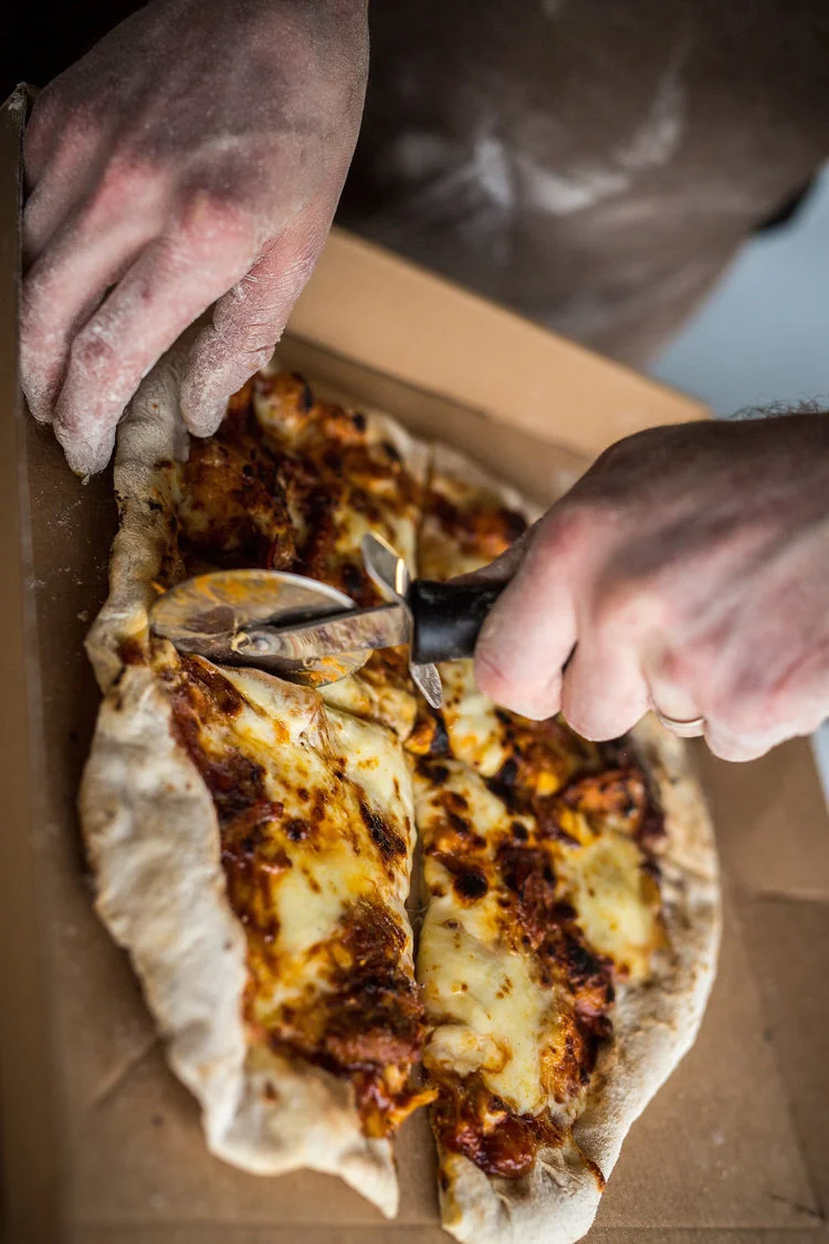 Person cutting a homemade pizza with a pizza cutter on a wooden board.