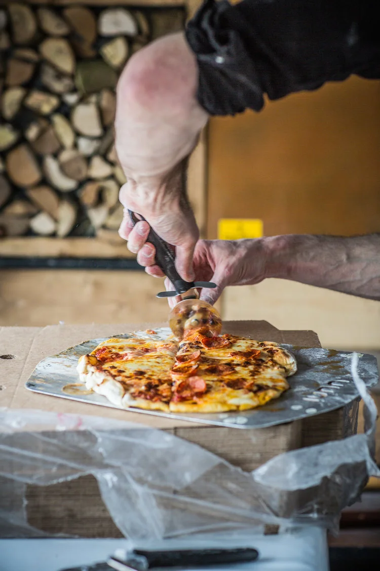 Person cutting pepperoni pizza with a pizza cutter