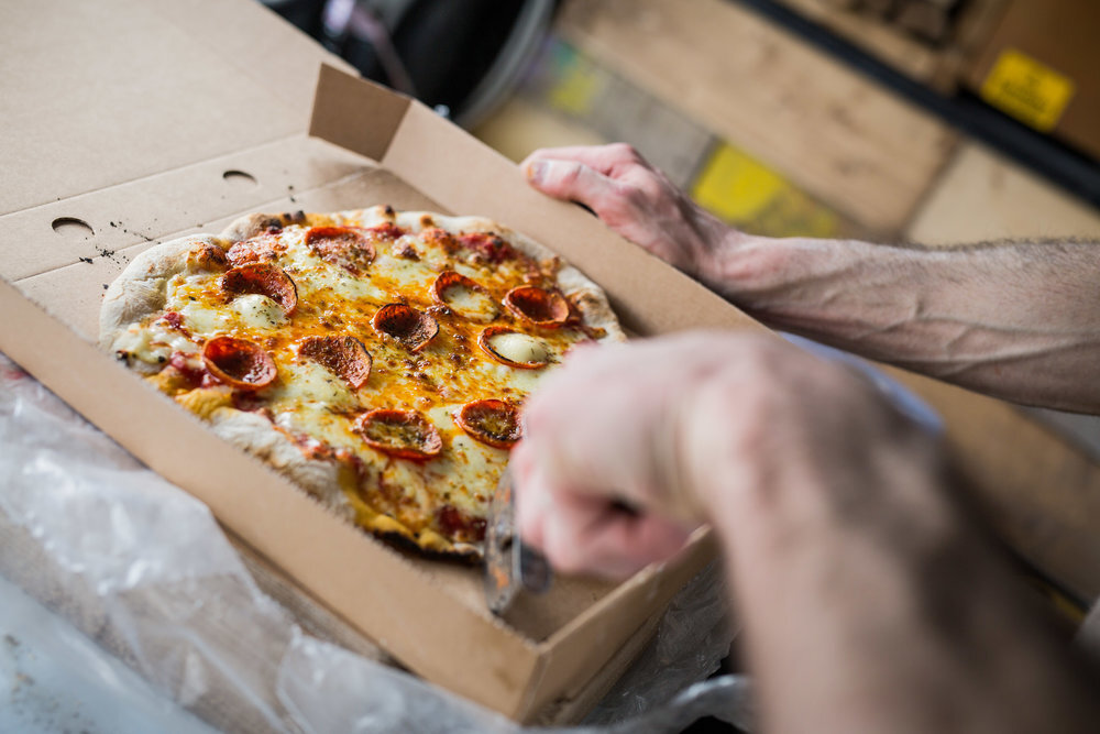 Person slicing a pepperoni pizza in a cardboard box