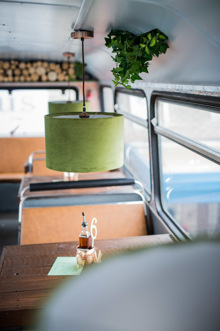 Interior of a converted bus with dining tables and green lampshades.