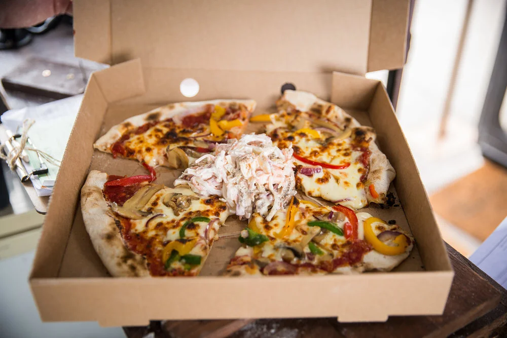 Open pizza box with pizza slices topped with various vegetables and a pile of coleslaw in the center.