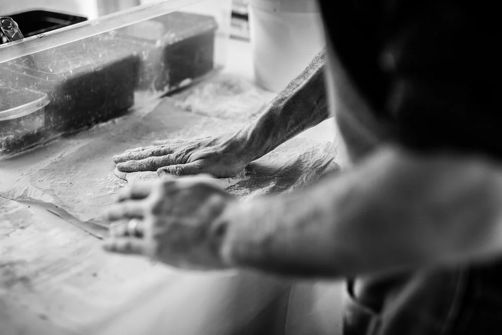 Black and white image of hands shaping dough on a floured surface