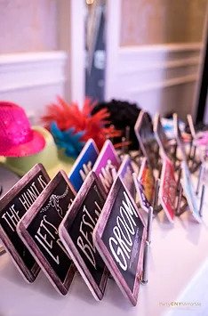 Colorful photo booth props including signs with text like "Groom," hats, and feather boas.
