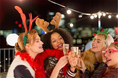Group of four friends celebrating, wearing festive accessories, holding champagne glasses, with city lights in the background.
