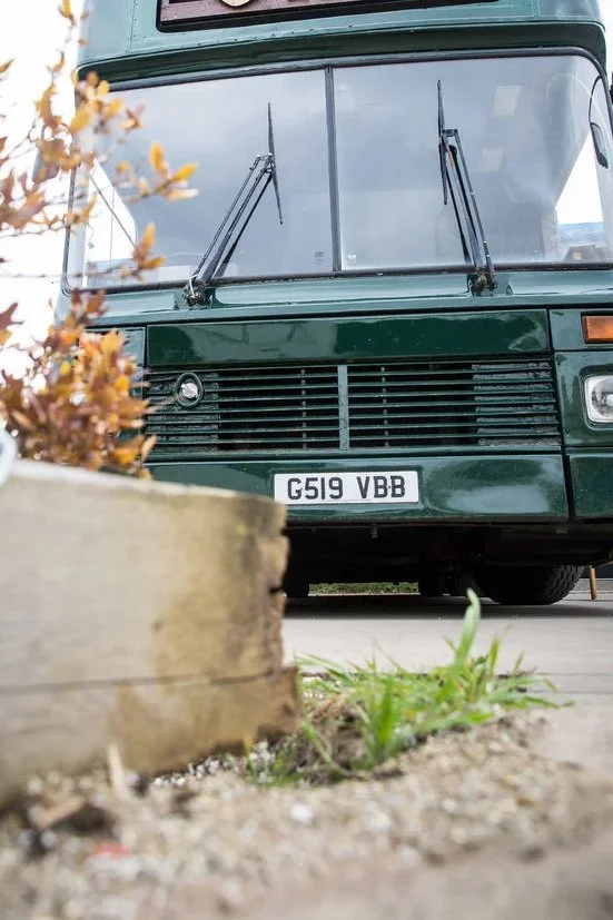 Front of a dark green vintage bus, with a wooden planter in the foreground.