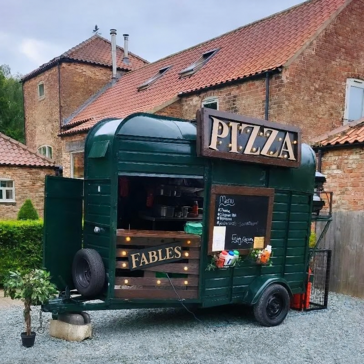 Fables green pizza horsebox with its serving hatch and menu board outside a brick venue