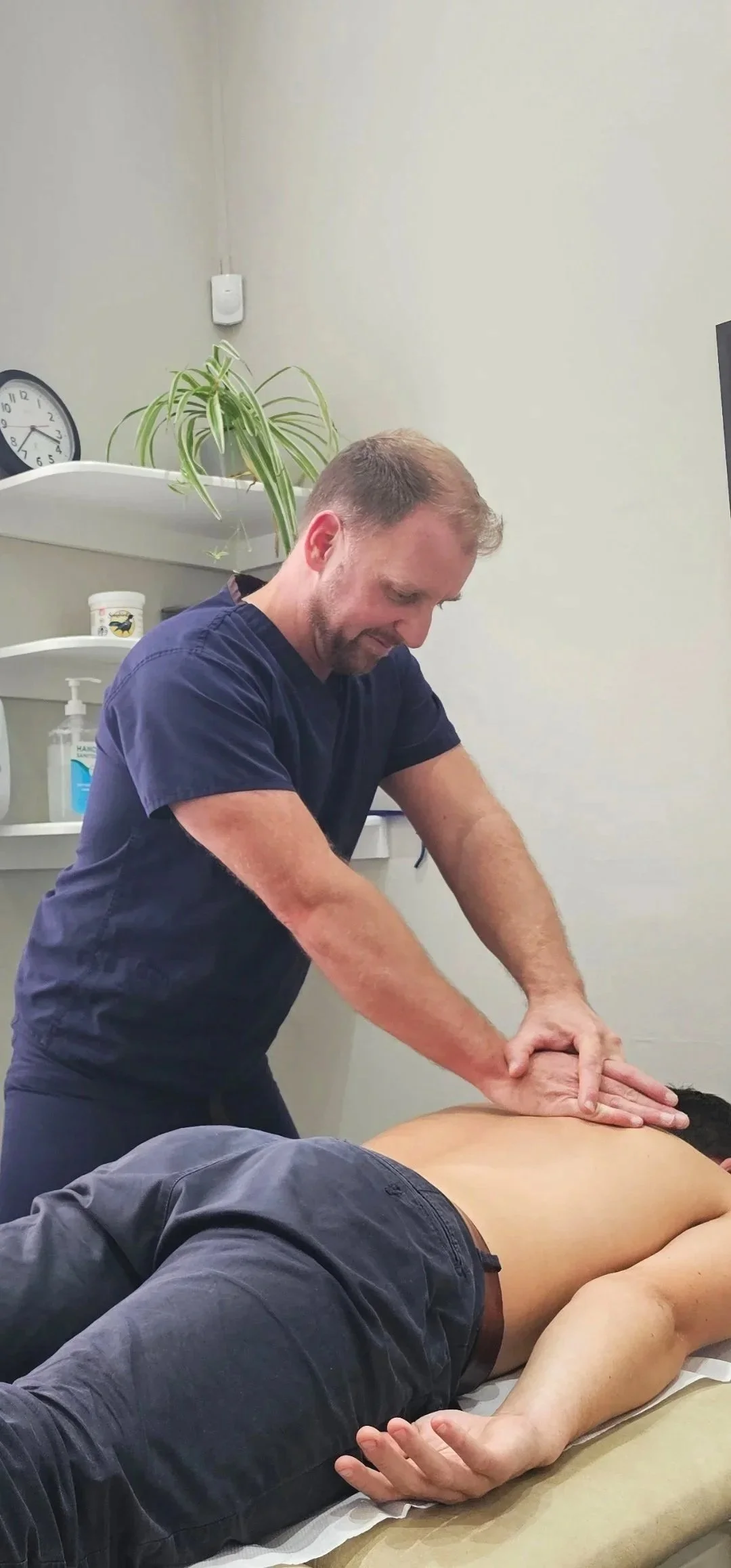 A physiotherapist treating a male patient lying face down on a treatment table in a treatment room.