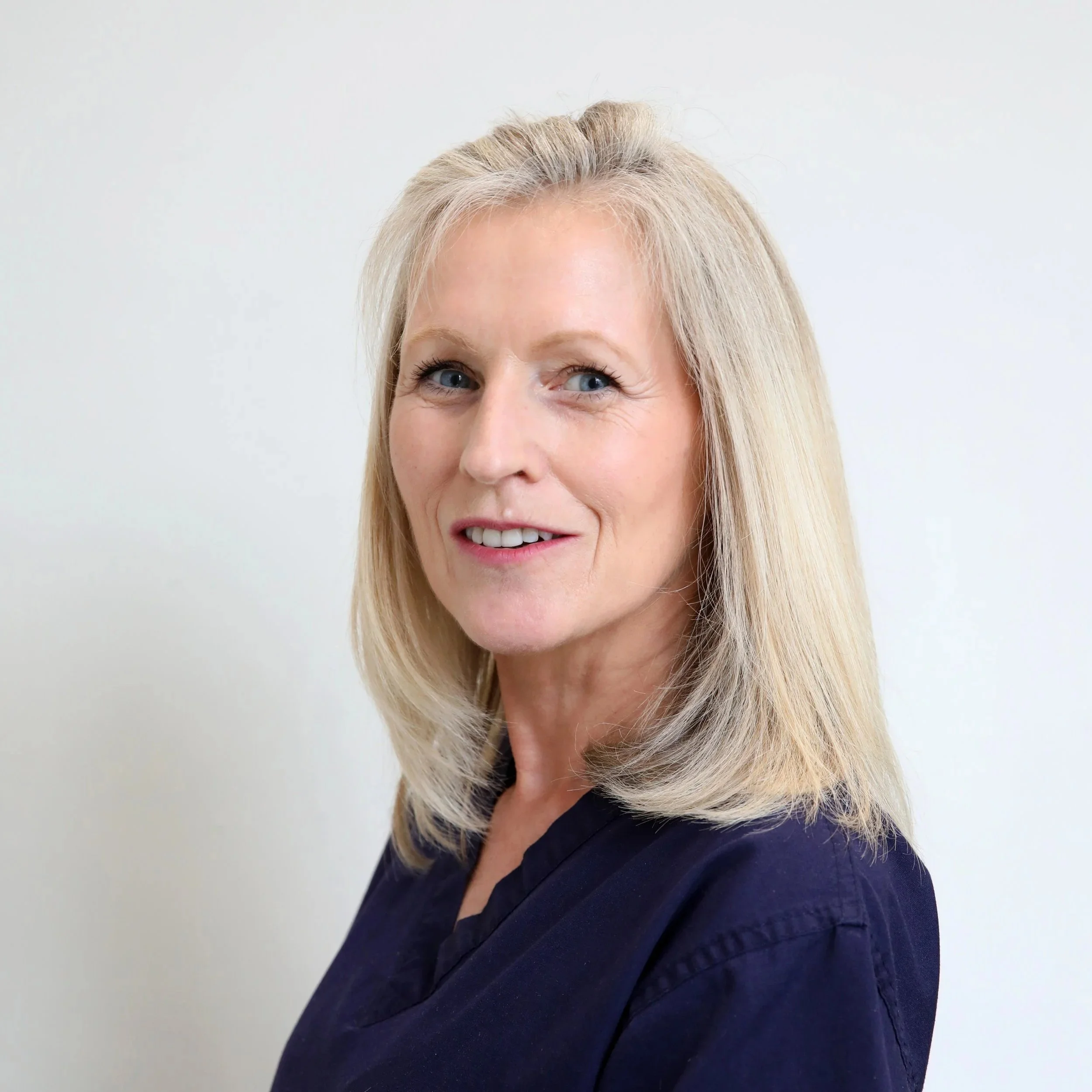 Close-up of a smiling woman with blonde hair, wearing a navy blue top, against a plain white background.
